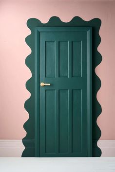 a green door with scallops on the side and pink wall in the background