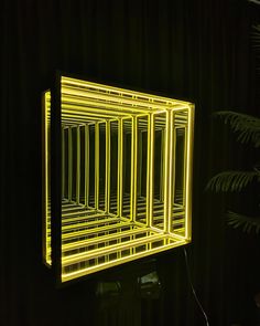 a yellow light that is on the wall in front of a black background with a fern