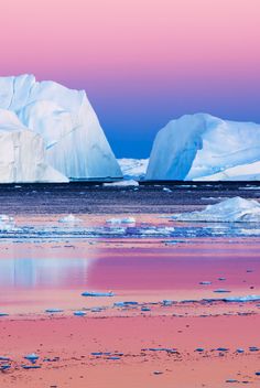 icebergs are floating in the water with pink sky and blue skies behind them