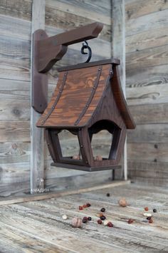 a bird house hanging from the side of a wooden wall with nuts scattered around it