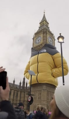 a person in a yellow jacket standing next to a tower with a clock on it