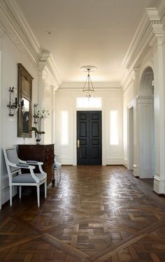 an empty hallway with wooden floors and white walls, two chairs on either side of the door