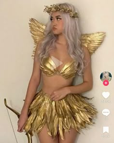 a woman dressed as a gold fairy standing in front of a wall with an arrow