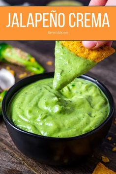 a hand dipping guacamole into a black bowl with tortilla chips