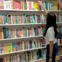 two girls reaching up to reach books on the shelves in a book store, with one holding her hand up