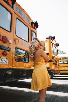 a woman in a yellow dress standing next to a school bus with her hand on her head