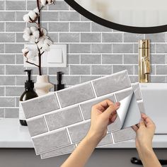 a person is placing tile on the wall in front of a sink and counter top