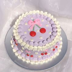 a purple cake with cherries on it sitting on a silver platter next to a white tablecloth