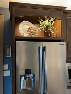 a silver refrigerator freezer sitting inside of a kitchen next to a wooden shelf filled with dishes