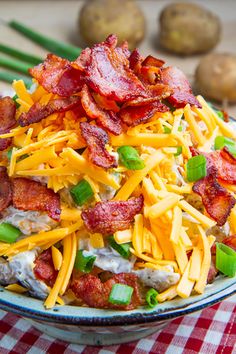 a blue and white plate topped with bacon, cheese and green onions next to potatoes