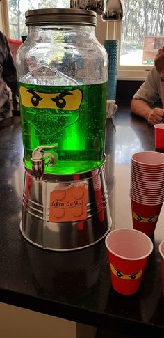 a table with cups and a large glass jar on top of it that has a green light in the middle