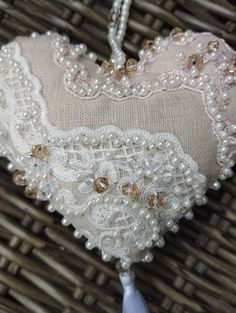 a heart shaped pillow with pearls and beads hanging from it's side on a wicker basket