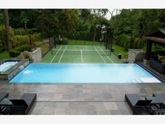 a large swimming pool in the middle of a backyard with lounge chairs and a tennis court