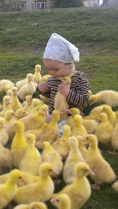 a baby sitting on the ground surrounded by small yellow ducks, with a paper hat on his head