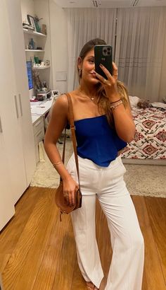 a woman taking a selfie with her cell phone in the mirror while wearing white pants and a blue top