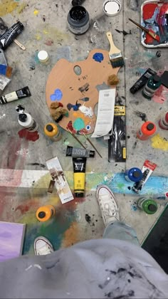 someone's feet on the ground covered in paint and art supplies