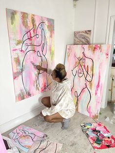 a woman kneeling down in front of two large paintings on the wall and painting them