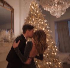 a man and woman are kissing in front of a christmas tree with lights on it