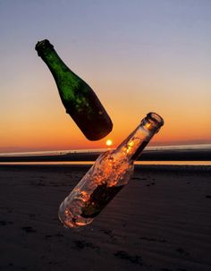 two empty beer bottles sitting on top of a beach next to the ocean at sunset