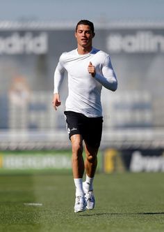 a man is running on the field in white shirt and black shorts with his hands behind his back