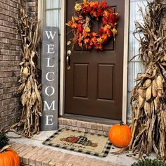 a front door decorated for fall with pumpkins and corn stalks