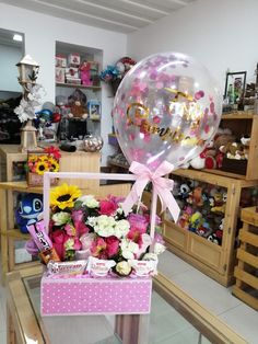 a pink box filled with lots of flowers on top of a glass table next to a bunch of balloons