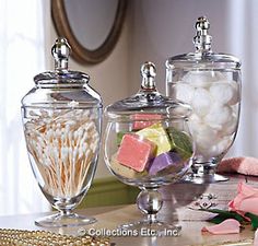 three glass jars filled with different types of candies and marshmallows on a table