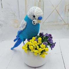 a crocheted bird sitting on top of a white vase filled with yellow and purple flowers