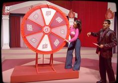 a man and woman standing in front of a wheel of fortune