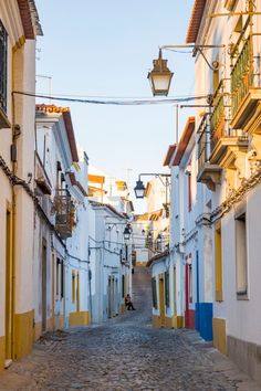 a cobblestone street lined with white buildings and yellow shuttered balconies