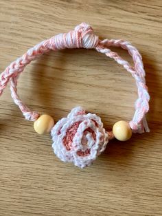 a pink and white bracelet with a flower on it sitting on a wooden table next to beads