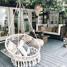 a white hanging chair on a porch with pillows and throw pillows in the back ground