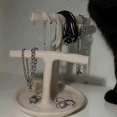 a black cat standing next to a white jewelry stand with rings and bracelets on it