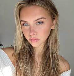 a woman with long blonde hair and blue eyes posing for a photo in front of a gray background