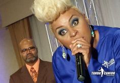 a woman with blonde hair is singing into a microphone while a man in a suit stands behind her