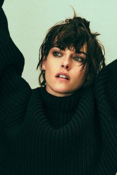 a woman with wet hair wearing a black turtle neck sweater and holding her hands behind her head