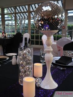 a table topped with candles and disco ball centerpiece next to a mirror vase filled with crystal balls