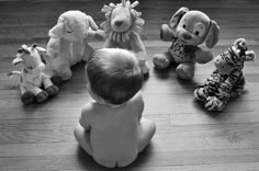 a baby sitting on the floor with stuffed animals around him and looking up at them