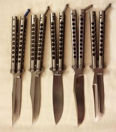 six knives are lined up in a row on a tablecloth with holes and rivets