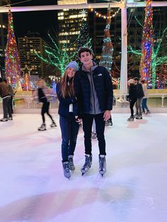 a man and woman standing on an ice rink in front of trees decorated with christmas lights