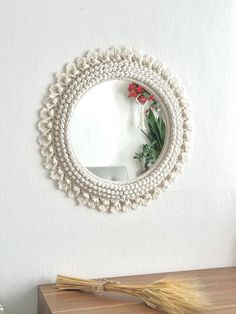 a round mirror hanging on the wall next to a wooden table and vase with flowers in it