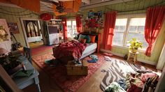 a bedroom with red curtains and a bed in the corner next to a window filled with clothes