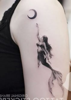 a woman with a tattoo on her arm is holding a fish in the air while standing next to a half moon