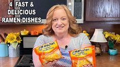 a woman holding two bags of ramen noodles in front of her kitchen counter with sunflowers