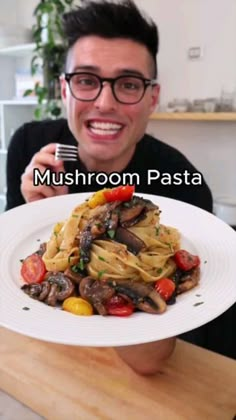 a man holding a white plate with pasta and mushrooms on it in front of him