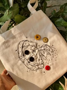 a hand holding a white bag with buttons on it and a drawing of a skull