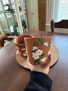 a person holding up two flower pots on top of a wooden table