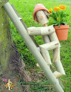 a wooden doll sitting next to a tree with flowers in it's potted head