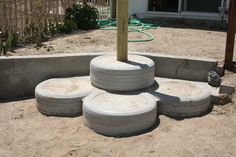 four white tires stacked on top of each other in the sand near a fence and building