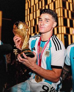 a young man holding a soccer ball and trophy in front of a tall building at night